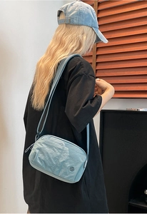 Close-up of light blue puffer crossbody bag with wrinkled nylon texture and metal logo