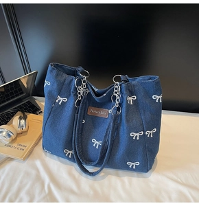Detail of blue denim tote bag featuring white bow embroidery and metal chain strap
