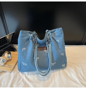 Detail of embroidered bows and leather patch on a blue denim tote bag with chain strap