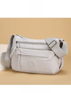 Detail view of light grey nylon cross-body bag with multi-zipper pockets and wide strap