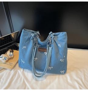 Close-up of blue denim tote bag featuring white bow embroidery and metal chain handles