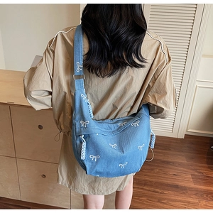 Detailansicht einer blauen Denim-Umhängetasche mit weiß gestickten Schleifen am Model
