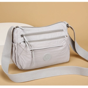 Close-up of multi-zippered grey nylon crossbody bag with wide adjustable shoulder strap