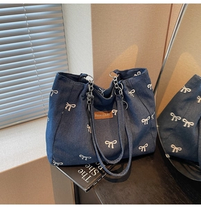 Detail view of denim tote bag with bow embroidery, chain handle and leather logo patch