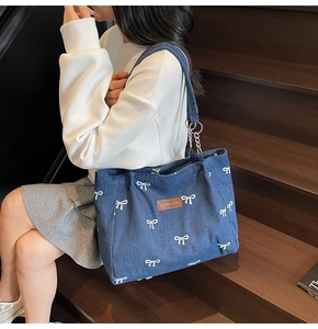 Detail of blue denim tote bag featuring white bow print and brown leather brand tag