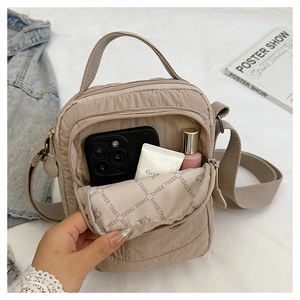 Close-up of beige nylon crossbody bag showing spacious interior with cosmetics and phone