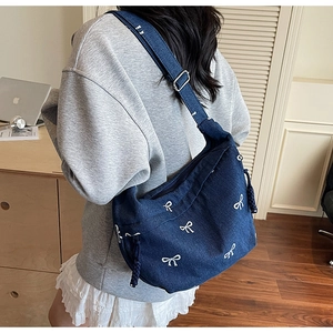 Detailaufnahme der dunkelblauen Denim-Umhängetasche mit weißen Schleifen-Stickereien