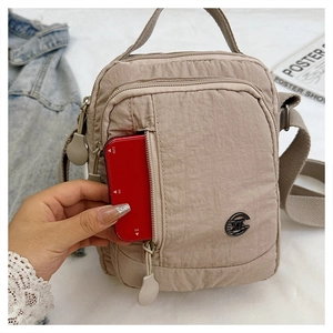 Beige nylon crossbody bag with multiple zip compartments showing device storage capacity