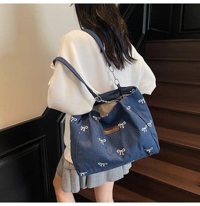 Detail of blue denim tote bag with white bow prints on a model at a staircase