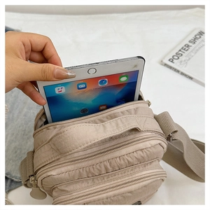 Detail showing the large capacity nylon crossbody bag fitting a tablet in its zip pocket