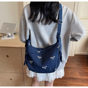 Detail der blauen Denim-Hobo-Tasche mit weißen Schleifen und breitem Schultergurt