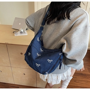 Blaue Denim-Umhängetasche mit weißen Schleifen-Stickereien an einem Model getragen
