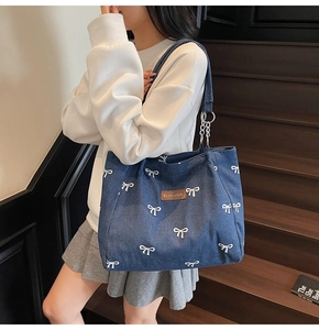 Detail of blue denim tote bag with white bow prints and metallic chain strap accents