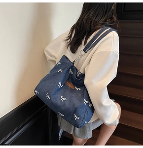 Detail of dark blue denim tote bag featuring white bow patterns and a brown leather patch