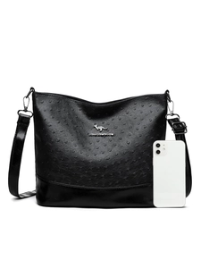 Detail of ostrich texture faux leather bag with metal logo next to a phone for scale