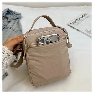 Detail of khaki nylon crossbody bag showing spacious front pocket with a smartphone inside