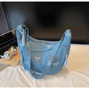 Detail der blauen Denim-Halbmondtasche mit weißer Schleifenstickerei und breitem Gurt