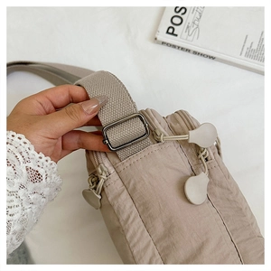 Detail of waterproof beige nylon crossbody bag featuring dual zippers and adjustable strap
