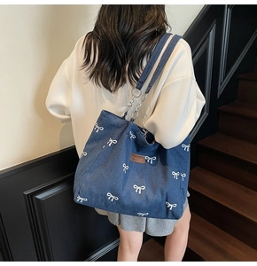 Detail of blue denim tote bag featuring white bow embroidery and a brown leather logo tag
