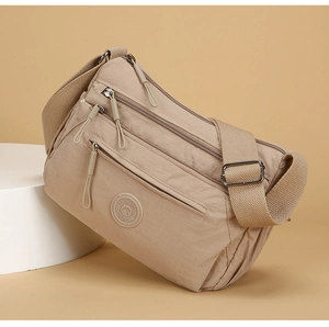 Detail of beige nylon crossbody bag showing multiple zipper pockets and rubber logo