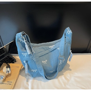 Detail der hellblauen Denim-Halbmondtasche mit weißer Schleifenstickerei in Alltagsszene