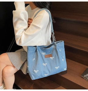 Close-up of light blue denim tote with white bow prints and metallic chain strap