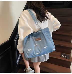 Detail of light blue denim tote bag with white bow patterns and brown leather logo label