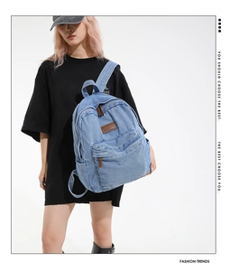 Detail of light blue denim backpack with brown leather logo patch and front zipper pocket