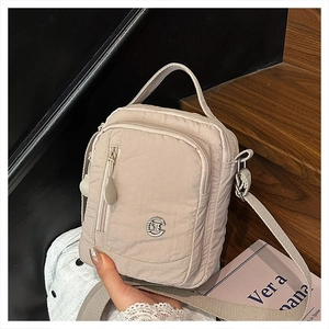 Detail view of cream nylon crossbody bag with multi-zipper pockets and silver logo