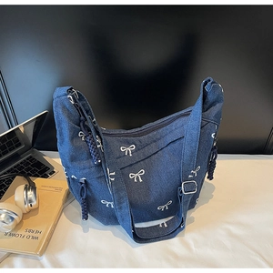 Detail der blauen Jeans-Umhängetasche mit weißer Schleifenstickerei und Reißverschlusseil