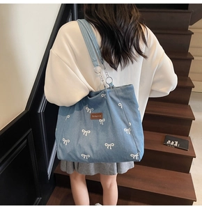 Detail of light blue denim tote bag with white bow embroidery and chain strap detail