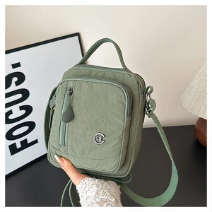 Detailed close-up of avocado green nylon crossbody bag with multi-layer zippers and metal logo
