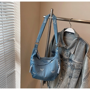 Detailansicht der blauen Denim-Umhängetasche mit weißen Schleifenmustern und verstellbarem Gurt