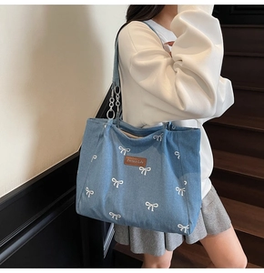 Blue denim tote bag with white bow prints and metallic chain strap shown on shoulder