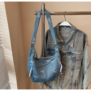 Detail der blauen Denim-Halbmondtasche mit weißen Schleifen-Stickereien und Seil-Reißverschluss