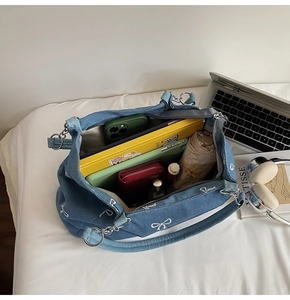 Detail of blue denim shoulder bag with white bow embroidery and spacious interior for storage