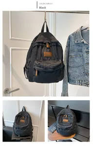 Detail of washed black denim backpack featuring front zipper pocket and leather logo