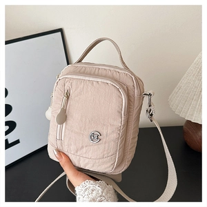 Detail view of beige pleated nylon crossbody bag with circular metal logo and zip pocket