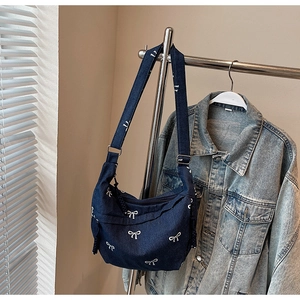 Detail der dunkelblauen Jeans-Umhängetasche mit weißen Schleifenmustern und verstellbarem Gurt