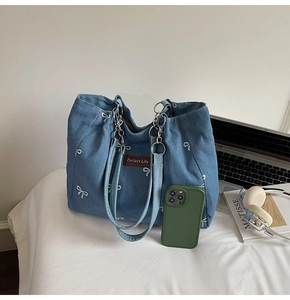 Detail of blue denim tote bag featuring white bow embroidery and silver chain strap