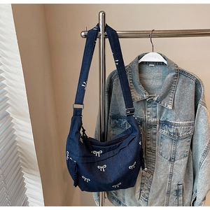 Detail der dunkelblauen Denim-Schultertasche mit weißen Schleifen und verstellbarem Gurt