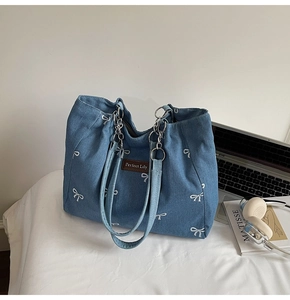 Detail of blue denim tote with white bow embroidery and stylish metal chain straps