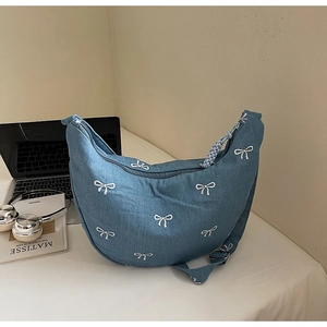 Detailaufnahme der blauen Denim-Halbmondtasche mit weißer Schleifenstickerei