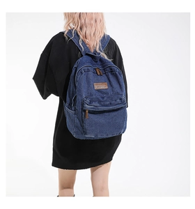 Detail shot of blue denim backpack showing textured fabric and brown leather logo patch