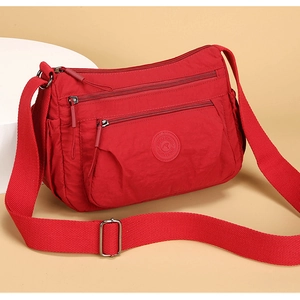 Macro detail of red nylon bag featuring multi-zipper layers and wide adjustable strap