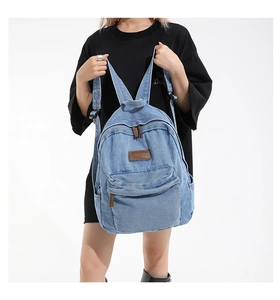 Detail of light blue denim backpack with brown leather logo patch and zip pulls