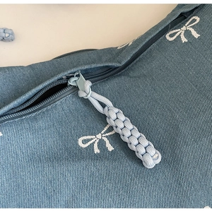 Detail der Jeans-Umhängetasche mit weißen Schleifenmustern und gewebtem Reißverschluss