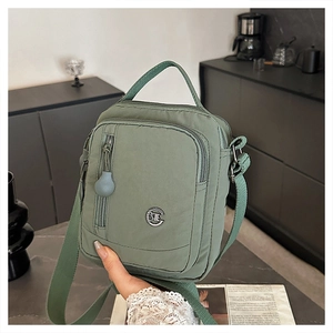 Detail of sage green nylon crossbody bag showing multiple zippers and metal logo