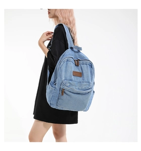 Detail view of denim backpack showing light blue washed fabric and leather logo tag
