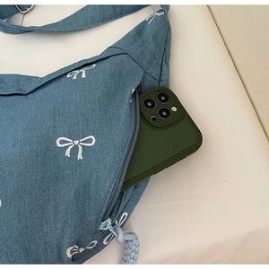 Detailansicht der Denim-Umhängetasche mit Schleifenstickerei und Smartphone-Vordertasche